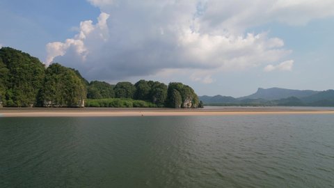 drone flying low and fast approaching a kayak on a sandbar along a river in Ao Thalane Krabi Thailand during a sun day with mountains and mangroves in distance.