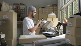Asian male small business owner using mobile app on smartphone checking parcel box. Warehouse worker, seller holding phone scanning retail dropshipping package postal parcel bar code. - Powered by Shutterstock - Get 15% off with code: PIKWIZARD15