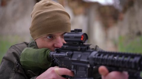 Portrait of concentrated man shooting with gun in slow motion as blurred soldier coming at background. Focused Caucasian young warrior in war zone in Ukraine. Military invasion concept