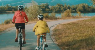 Family fun outdoors. Mother and son ride a bike. Happy cute boy in helmet learn to riding a bike in park on green meadow in summer day at sunset time. Family weekend. 4K video, Slow motion