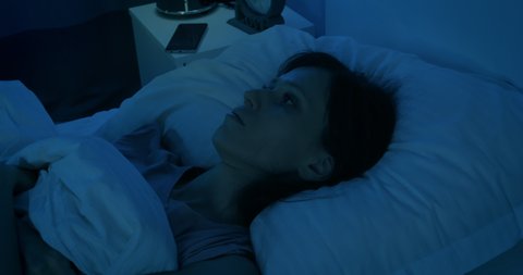 Young woman lying on a pillow at night and suffers from insomnia. Sleepless night. Female lying in bed and cannot fall asleep