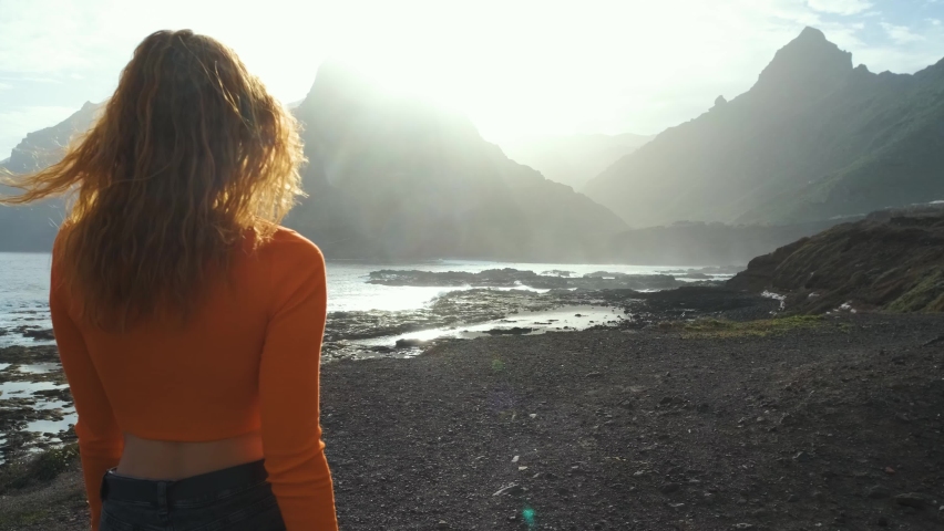A woman walks next to the ocean and raises her hands up and enjoying the moment on volcanic beach of the Canary island of Tenerife. Beautiful landscapes in the north of Tenerife island. Go Everywhere