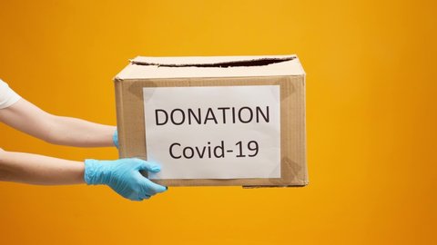 Human hands holding cardboard box with Coronavirus Donations against yellow background