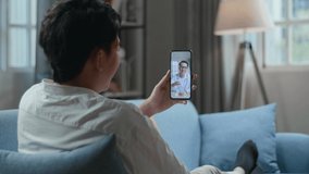 Man Having Video Call With A Doctor On Smartphone While Lying On Sofa In The Living Room 
