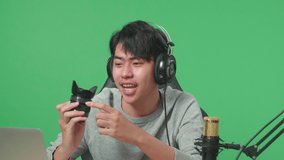 Close Up Of Smiling Asian Man With Computer Reviewing Camera Len While Sitting In Front Of Green Screen Background
