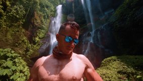 Athletic muscular man travel in tropical rainforest and enjoy beautiful waterfall against backdrop of nature background