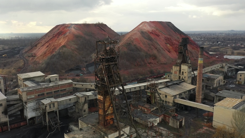 Old coal mine elevator and slag heaps on a cloudy day. Vintage coal mining shaft building, weathered factory and constructions. Fossil fuel and minerals mining heavy industry landscape with terrikons. Royalty-Free Stock Footage #1089048833