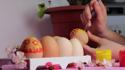 The child paints Easter eggs herself with a brush in red and yellow colors