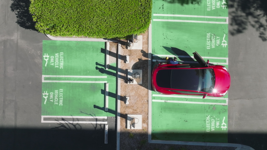 EV eco friendly electricity powers cars. Still drone shot above man unplugging charging cord from red SUV sedan electric vehicle after battery fully charged. Aerial of electric car vehicles recharging Royalty-Free Stock Footage #1089053155