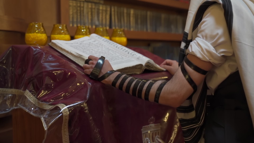A Jew prays in the synagogue. A man stands near the presidium and reads a book. The camera is getting closer. Royalty-Free Stock Footage #1089054379