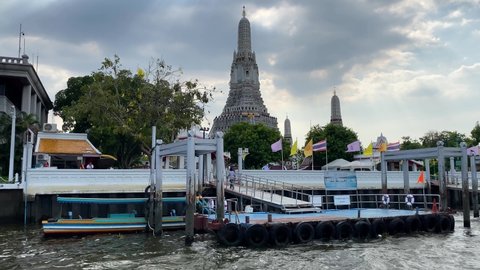 Bangkok, Thailand - April 4, 2022: People wait to board a ferryboat in front of Wat Arun Buddhist temple located in the bank of Chao Phraya river.