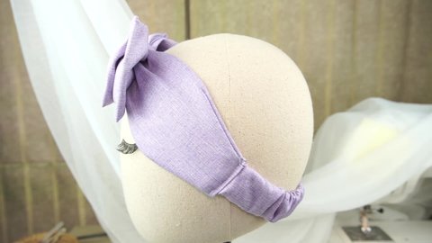 A mannequin wearing headband with bow pattern made out of cotton fabric in soft lavender color, great as hair accessories for babies and kids.