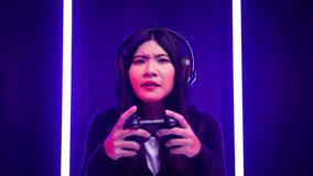 Gamer with controller winning victory moment. Young asian pretty woman sitting on chair with computer pc. Female Professional Streamer wearing headphone playing game online in dark room neon light.