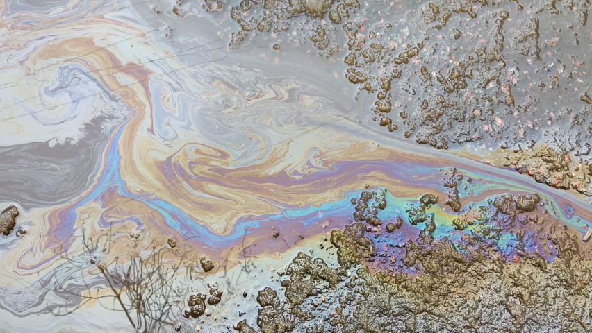 A multicolored spot from oil or gasoline spreads over a puddle on the asphalt. The problem of ecology and water pollution in the metropolis. Royalty-Free Stock Footage #1089056363