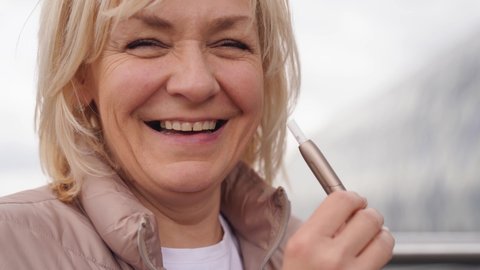 Middle aged blonde European woman smoking heated tabacco e-cigarette outdoors on the street. Alternative smoking way