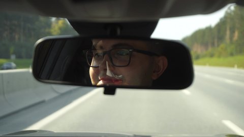 Face of man driving car seen in the rear view mirror. Man in glasses driving on highway