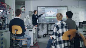 Teacher Pointing at Big Screen and Holding Lesson while Robotic Arm Moving Nearby. Diverse Group of Young Engineers Sitting at University and Asking. Computer Science Education Concept - Powered by Shutterstock - Get 15% off with code: PIKWIZARD15