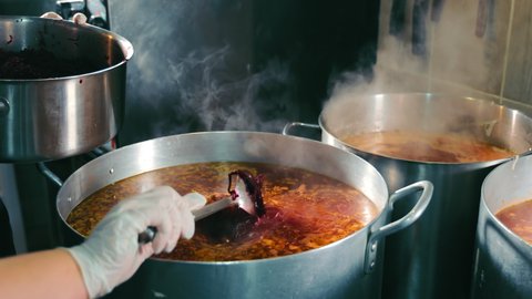 Preparation of Ukrainian traditional red beet borsch dish. The chef adds red beets to a large bowl. Cooking borscht in the restaurant for a large number of servings.