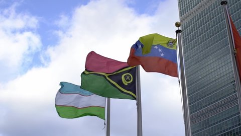 Manhattan, USA - November 2021: Uzbekistan, Venezuela and Vanuatu flags flying in the wind at United Nations in Manhattan, New York City. Slow motion flags waving