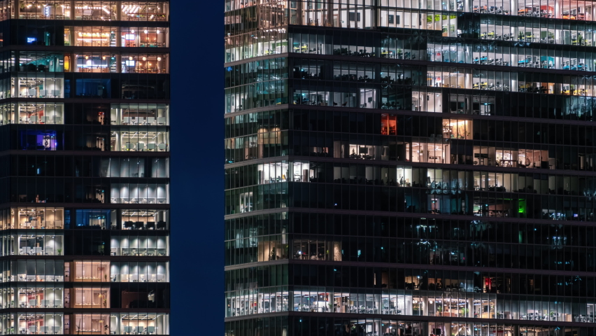 Time-lapse blinking office windows lights in business center building facade, people working late night. Corporate business, high skyscraper glass surface. Light in building windows turn on and off