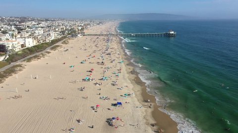 MId-Day Lateral View of the Manhattan Beach Full of Beach Goers Swimming and Surfing in California USA - Forward Panning Aerial Shot