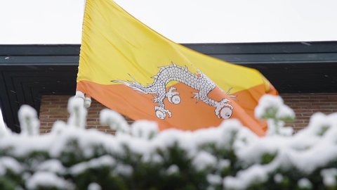 Close up slow motion shot of Bhutan flag waving with the wind in snowy city center