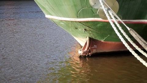 Lower part of boat stern or poop in the river Weser in Bremen, Germany. Boat hotel Alexander Von Humboldt is a masted ship. Metal hull frame is green and red. Hawser out of hawsehole to moor ship.