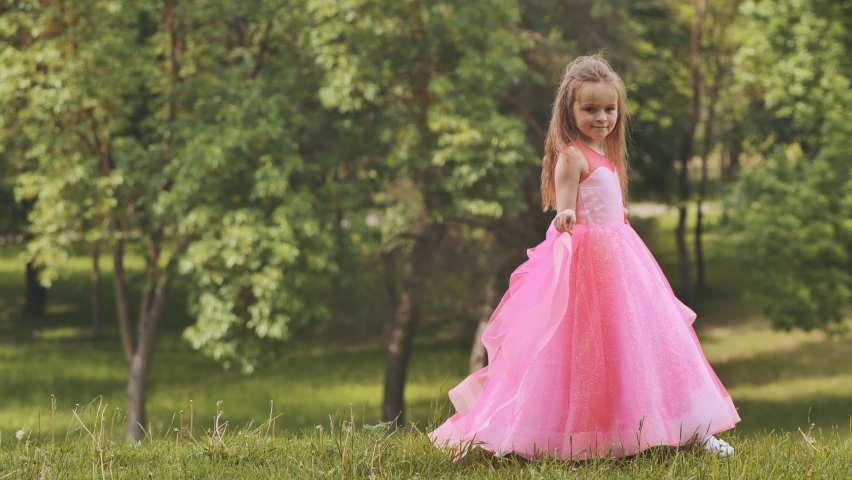 A girl in a pink princess dress is walk in the park.