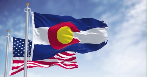 The Colorado state flag waving along with the national flag of the United States of America. In the background there is a clear sky. 4k resolution