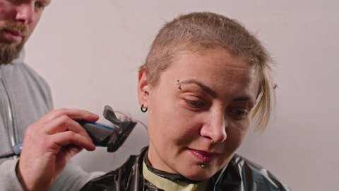 an adult man cuts a sad woman bald with a typewriter. Ukrainian female soldier.