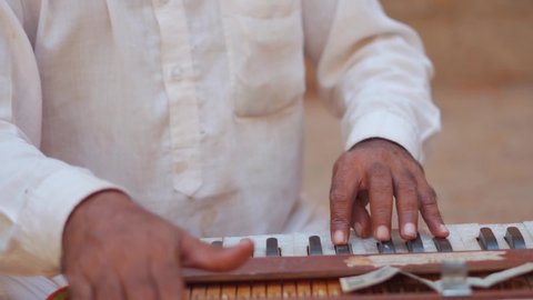 Closeup shot of Hands of an Indian street performer playing harmonium by pressing keys while singing at Jaisalmer in Rajasthan, India. Street performer playing harmonium in the side of the road. 