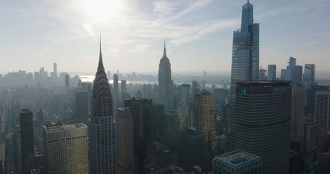Forwards fly above buildings against sun. Hazy view of historic Chrysler and Empire State Building and modern One Vanderbilt. Manhattan, New York City, USA in 2021