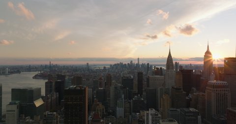 Aerial descending footage of large city at dusk. Various tall buildings against sunset sky. Iconic Chrysler and Empire State buildings. Manhattan, New York City, USA in 2021