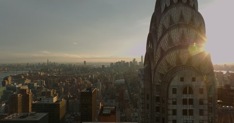 Fly around top of Chrysler Building. Revealing aerial view of cityscape in sunset time. Manhattan, New York City, USA in 2021