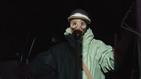Worker wearing respirator and helmet dancing hands up at abandoned building in dark room