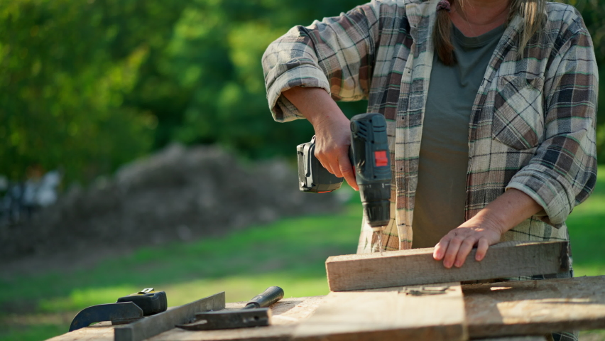 Happy handy female carpenter working in carpentry diy workshop outdoors with drill.