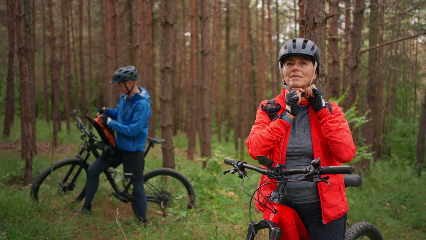 Senior couple bikers outdoors in forest in autumn day.