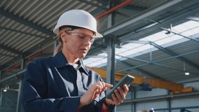 Serious woman engineer with helmet and goggles uses mobile phone in factory. In the background details of a metalworking project - Powered by Shutterstock - Get 15% off with code: PIKWIZARD15