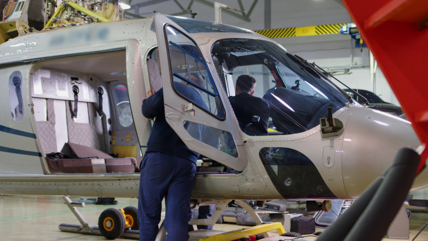 unrecognizable mechanic is turning nut on helicopter. Large helicopter that is in hangar for repair and rebuild, disassemble of vehicle, maintenance of air vehicle.