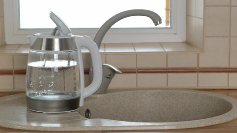 Woman turning off the faucet with filtered water that was poured into the glass kettle. Sink with two taps, plain and filtered water. Filter system or osmosis, water purification. 4K video.