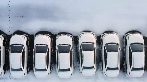 Aerial top down view of the car park of a car dealership or customs terminal with rows of new white cars standing on a snow-covered parking lot