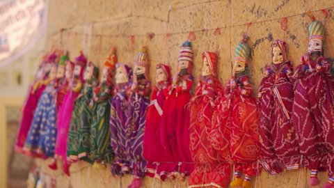 Closeup shot of colorful human shaped Puppets wearing colorful traditional clothes hanging against the wall in Jaisalmer, Rajasthan, India. View of traditional homemade dolls in streets of Rajasthan.