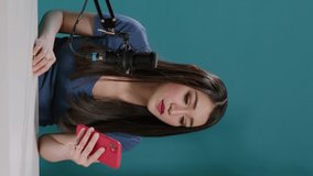 Vertical video: POV of content creator reading comments on camera, answering questions with smartphone. Female vlogger filming video for social media channel, using mobile phone. Tripod shot.