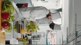 Vertical video: Authentic cook cutting coleslaw salad to make food recipe, using fresh ingredients in restaurant kitchen. Male chef using knife on cutting board to slice celery for gourmet dish.