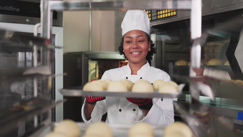 Smiling african  female bakers looking at camera.Chefs  baker in a chef dress and hat, cooking together in kitchen.Professional cooks in uniform preparing meals for a restaurant. Royalty-Free Stock Footage #1089092545