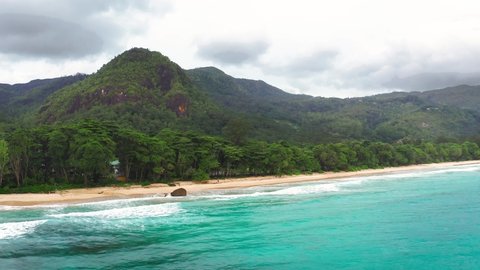 Flying above Grand Anse Beach at the Mahe Island, Seychelles, with turquoise water of the Indian Ocean, mountains and rain forests in the background. 4K UHD video.