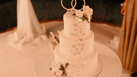 A beautiful wedding cake decorated with gold rings banquet hall close-up. White cake bread for wedding party at night. The concept of festive desserts. Three-tiered minimalist wedding cake.