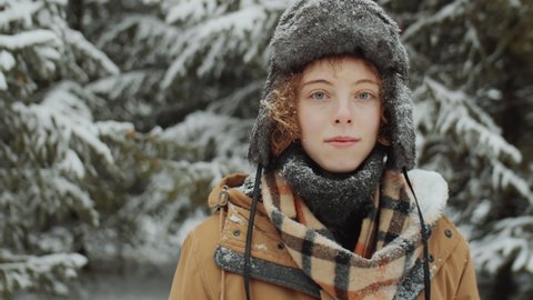 Portrait of young Caucasian woman standing in woods on winter day and posing for camera
