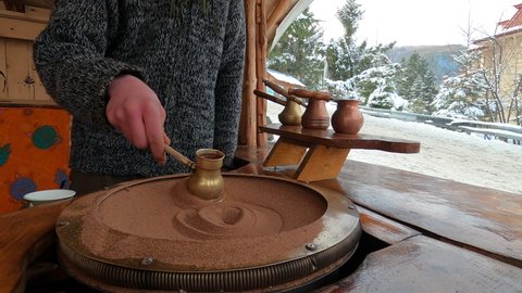 Preparing Turkish coffee in a copper cezve on hot sand is an old Turkish way of brewing a coffee drink. A man brews coffee against the backdrop of winter mountains.