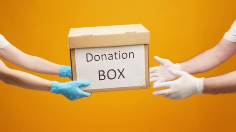 Human hands in gloves passing Donation box to the other one against yellow background, Coronavirus donations help